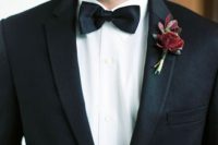 a classic burgundy boutonniere of a bloom and leaves is a touch of color to the monochromatic look