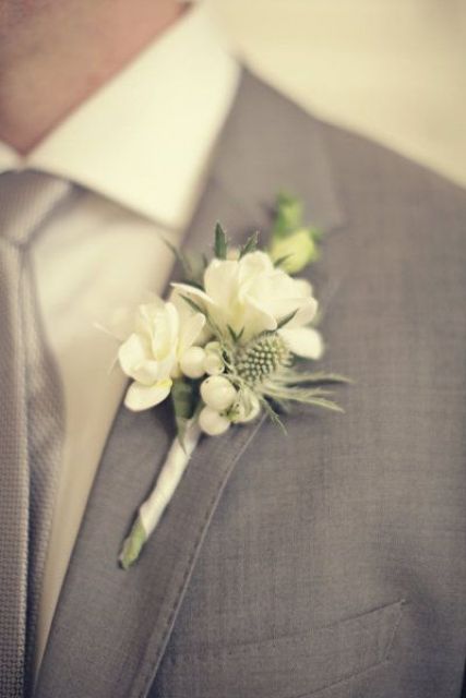 a classic neutral boutonniere of white blooms, berries and thistles is a chic and cool idea to try
