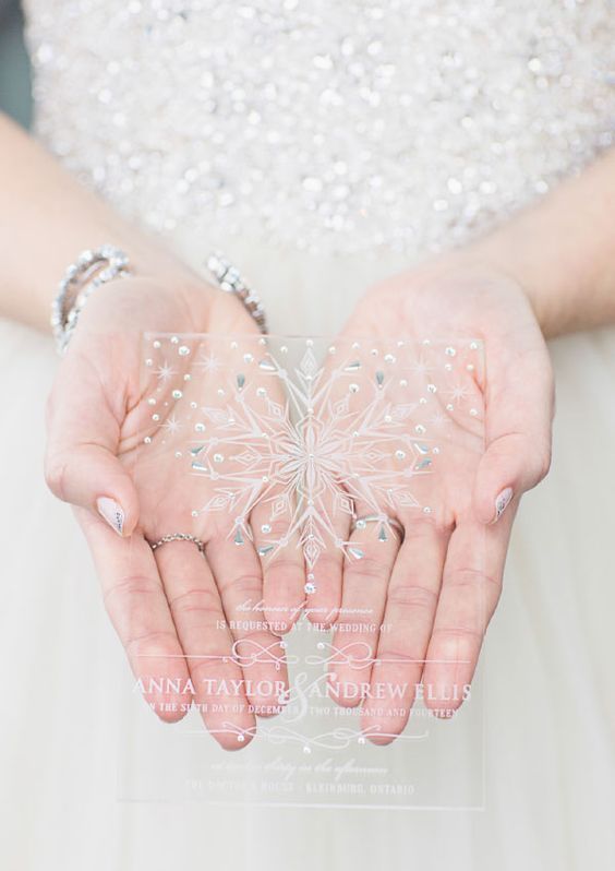 a clear acrylic wedding invitation with a rhinestone snowflake and some calligraphy for a winter wedding