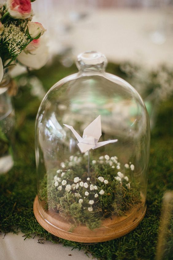 a delicate wedding centerpiece of a cloche with moss and baby's breath and a single white paper crane is a lovely idea