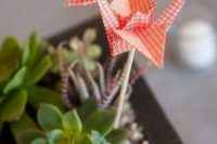 a delicate wedding centerpiece of potted succulents topped with a single coral paper crane is cool