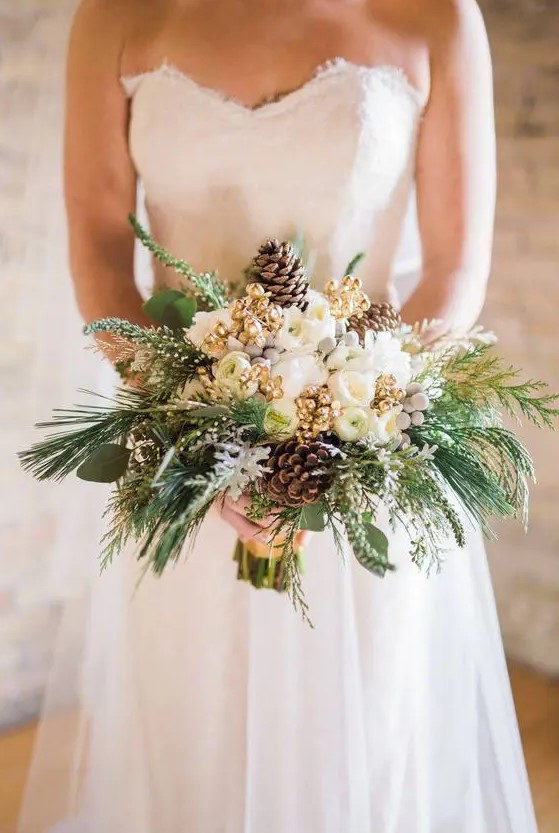 a glam and shiny winter wedding bouquet of white blooms, gilded berries, pinecones, evergreens and greenery is a lovely idea