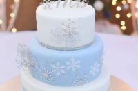 a glam white and light blue winter wedding cake decorated with silver and white snowflakes, topped with rhinestone ones and a calligraphy topper