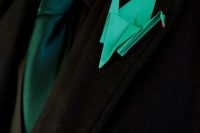 a groom’s look with a black suit, black shirt, a green tie and an emerdal origami boutonniere is a lovely and bold idea