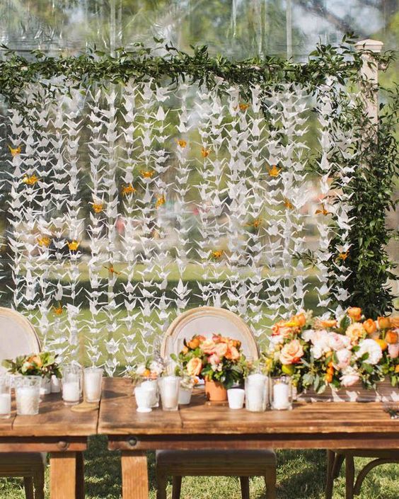 a lovely outdoor wedding reception with orange blooms and candles, with paper cranes and greenery is amazing