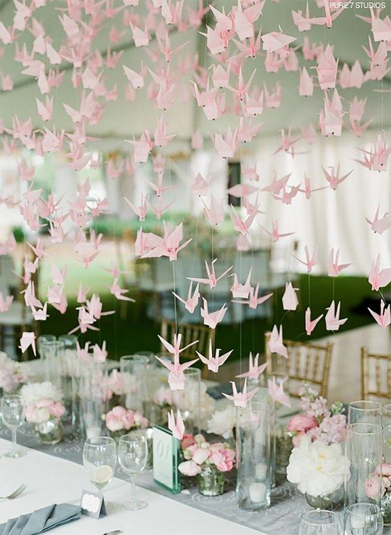 a lovely wedding reception space with pink and white blooms and candles, with pink origami crane garlands over the table