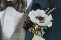 a lush wedding boutonniere with a white and deep purple bloom, greenery and a feather for a vintage look