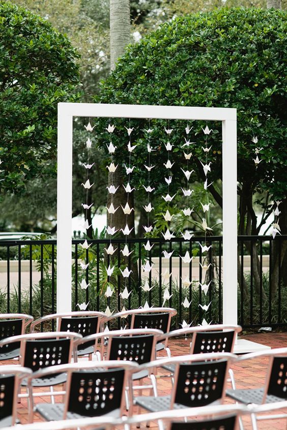 a modern wedding cermeony space with a simple white arch with white paper cranes and modern chairs is amazing