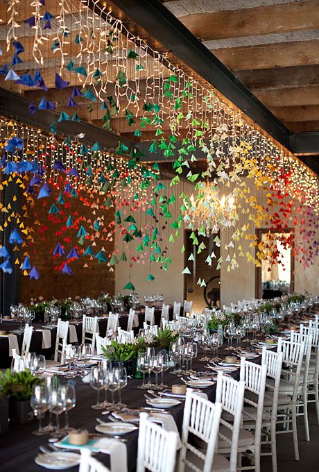 a modern wedding reception space with greenery and candles and lots of colorful origami over the tables