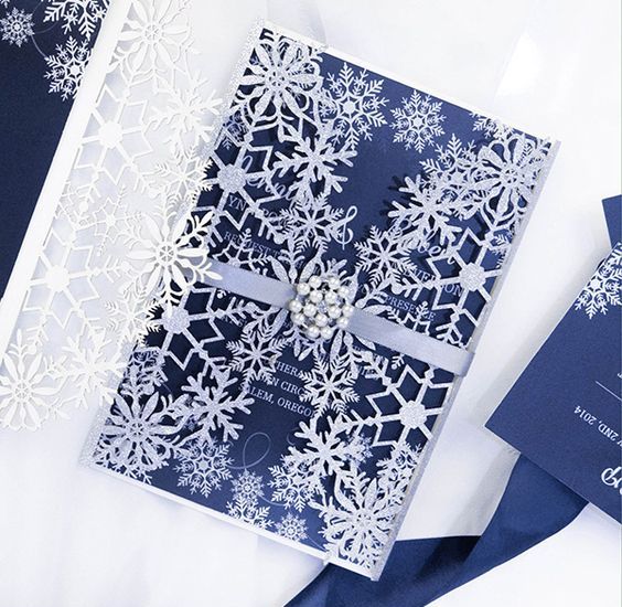 a navy and white wedding invitation suite with cutout snowflakes and pearl brooches to accent it is a very wintry-like idea