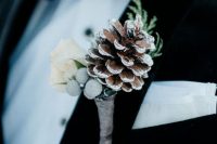 a neutral wedding boutonniere of berries, a snowy pinecones, white blooms and greenery