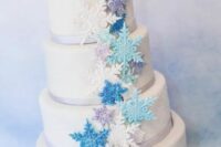 a neutral wedding cake with lilac ribbon, white, turquoise, blue and lilac snowflakes is a chic and bold idea for winter