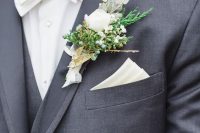 a neutral winter wedding boutonniere with berries, greenery and white blooms, sticks and a white ribbon