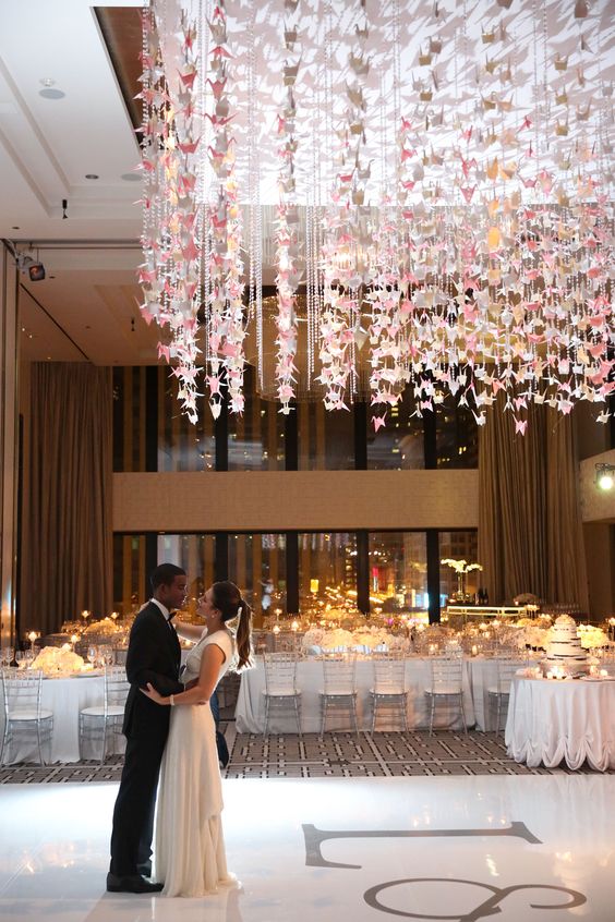 a refined neutral wedding reception space with lots of blooms and garlands of pink origami cranes and crystals over the dancing floor