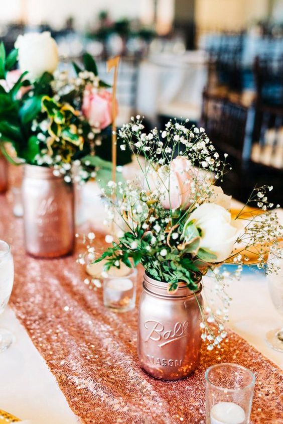 a rose gold sequin table runner and rose gold jars with white, pink blooms and baby's breath for a chic look