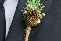 a rustic wedding boutonniere of a pinecone, berries, greenery and twine wrap for a cozy and comfy outfit