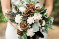 a rustic winter wedding bouquet of white blooms, pinecones, greenery, berries and feathers is a great idea