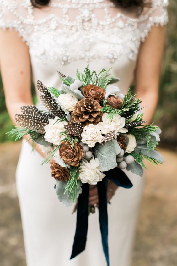 a rustic winter wedding bouquet of white blooms, pinecones, greenery, berries and feathers is a great idea