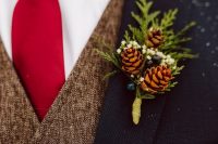 a rustic winter wedding boutonniere of pinecones, white blooms, greenery and berries for a cozy feel
