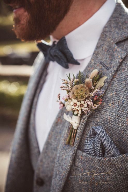 a rustic winter wedding buttonhole with white and blush blooms, berries, leaves and feathers for a boho feel
