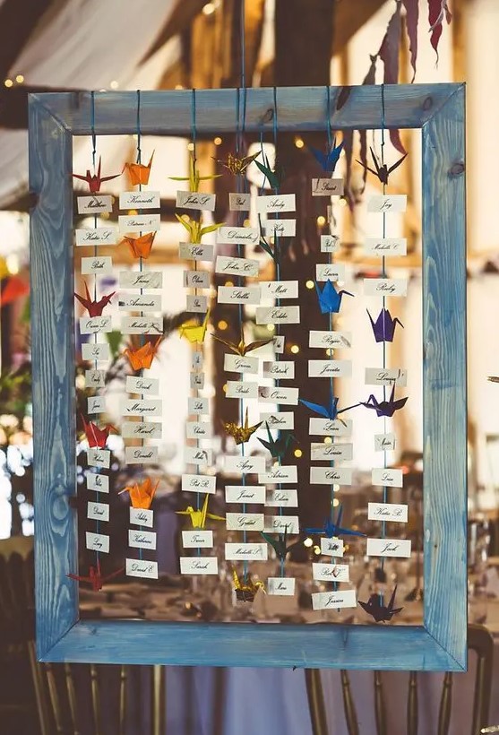 a seating plan of a wooden frame, cards and colorful paper cranes can be easily DIYed