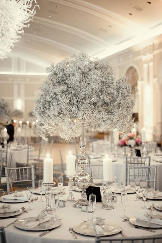 a silver wedding tablescape with a white baby's breath tall centerpiece, pillar candles, silver chargers and candleholders