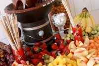 a small yet chic chocolate fountain bar with lots of fruits, berries, cookies ad pretzels plus a large pineapple