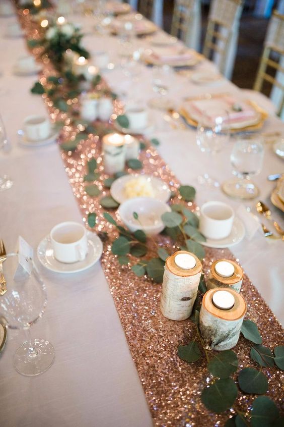 a sparkly rose gold table runner with tree candle holders and eucalyptus for a glam yet rustic wedding
