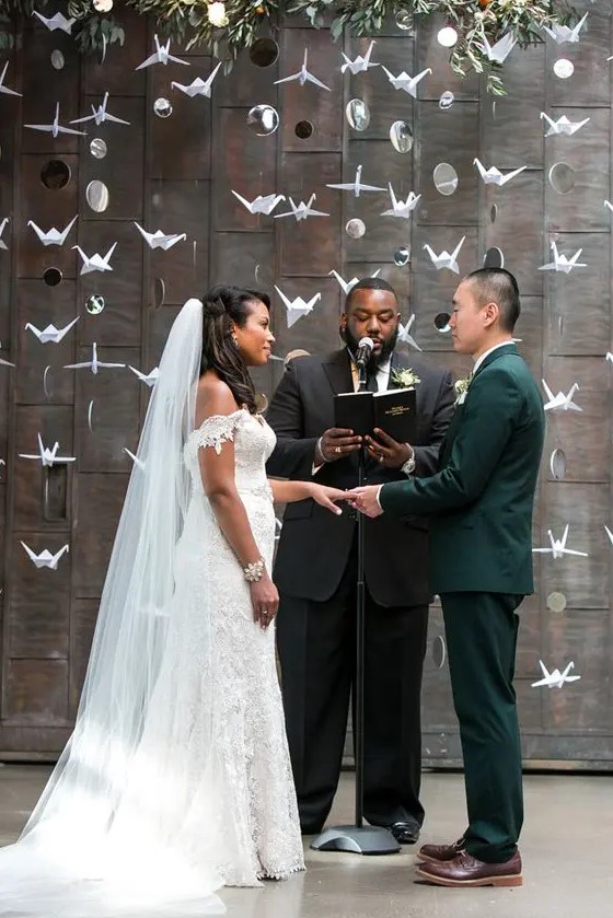 a wedding backdrop made of paper cranes and couple's photos plus greenery on top