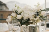 a wedding centerpiece of a mercury glass vase and white blooms plus silver sequins on the table is amazing