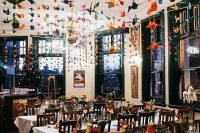 a wedding reception space with lots of colorful origami crane garlands over it that echo with the bold blooms and add interest to the space