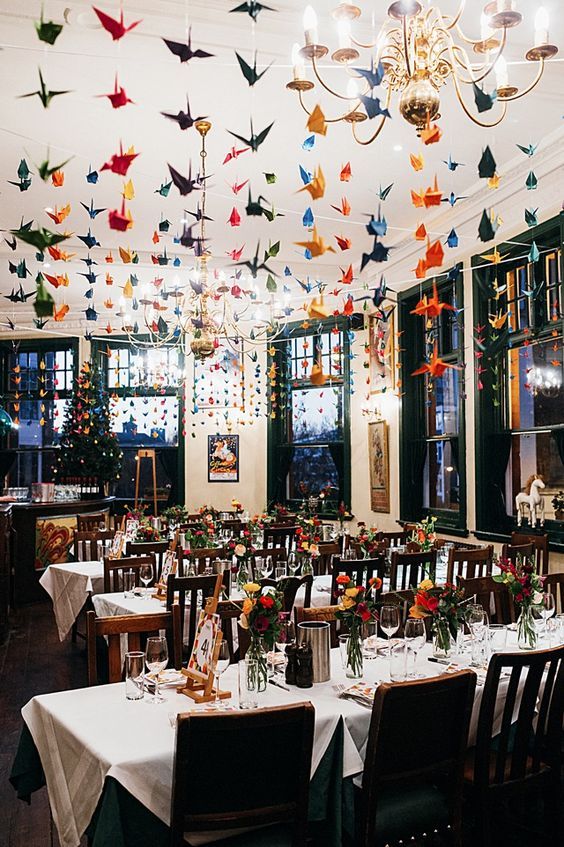 a wedding reception space with lots of colorful origami crane garlands over it that echo with the bold blooms and add interest to the space