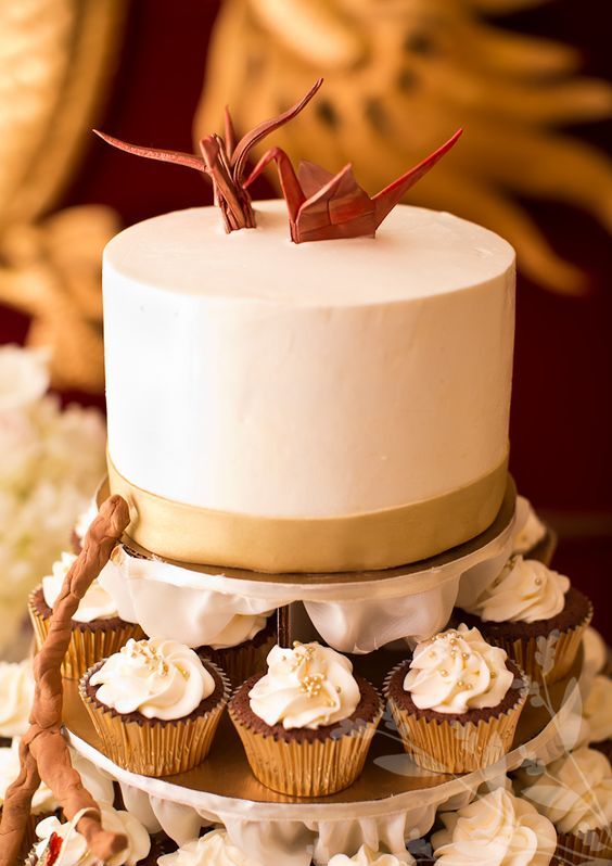 a white buttercream wedding cake with a gold ribbon and red sugar origami cranes is a lovely idea for a modern wedding