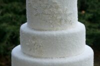 a white frosted wedding cake decorated with white snowflakes and sparkles is a chic and lovely idea for a winter wedding
