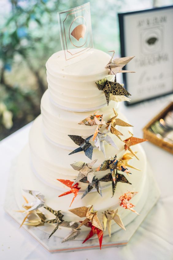 a white wedding cake decorated with colorful paper cranes is a fun and cute idea for a relaxed wedding