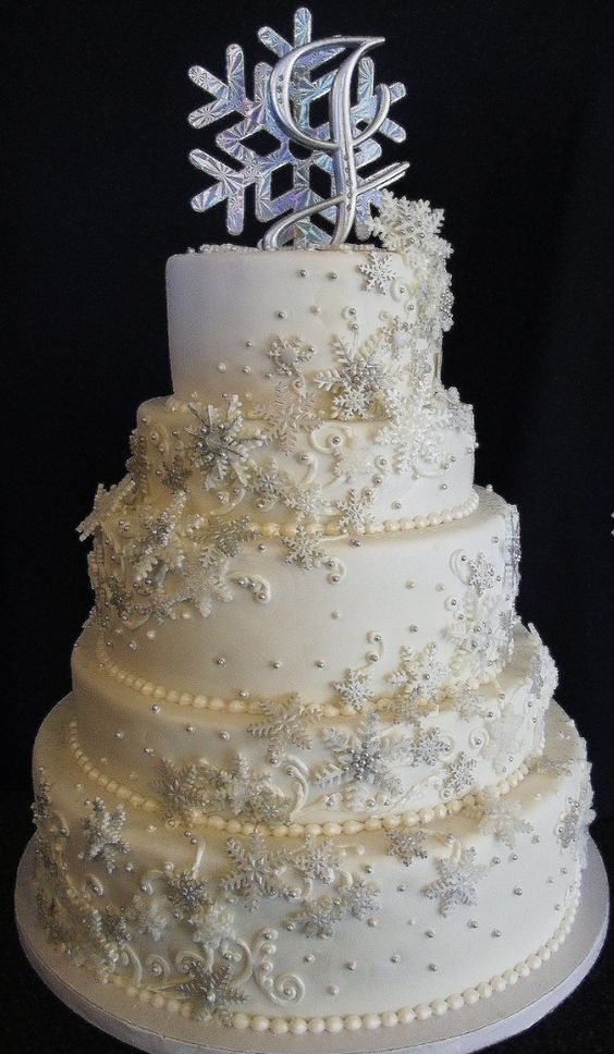 a white wedding cake decorated with edible beads, snowflakes and a monogram plus a holographic snowflake on top