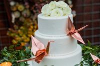 a white wedding cake decorated with pink origami cranes and white ranunculus is a chic and stylish idea