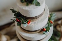 a white wedding cake with greenery, fir and red berries for a winter or Christmas wedding