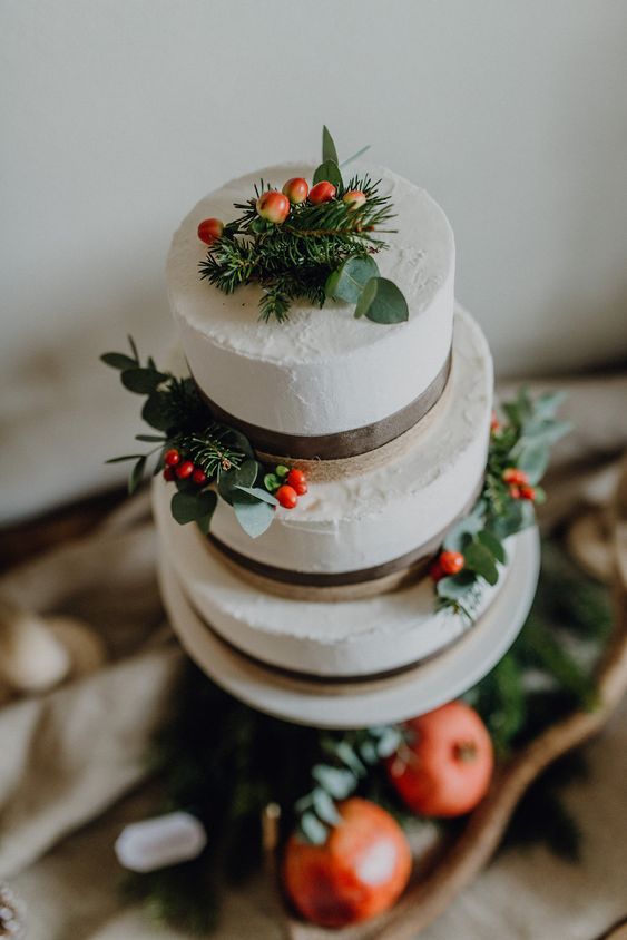 a white wedding cake with greenery, fir and red berries for a winter or Christmas wedding