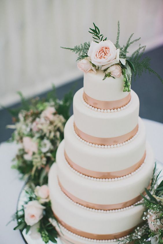 a white wedding cake with rose gold ribbons and fresh blooms and greenery on top is an elegant and romantic idea