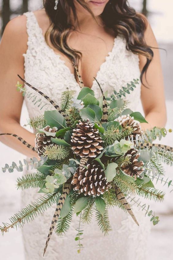 a winter wedding bouquet made of greenery, evergreens, feathers and snowy pinecones is a cool idea for a woodland bride