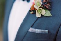 a winter wedding boutonniere with berries, greenery, rust and pink blooms for a bold accent