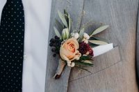 a winter wedding boutonniere with blush and peachy blooms, berries, greenery and a burgundy flower