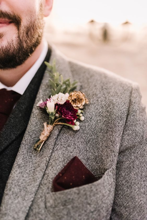 a winter wedding boutonniere with pink, burgundy and white blooms, berries, greenery and pinecones is a bold accent