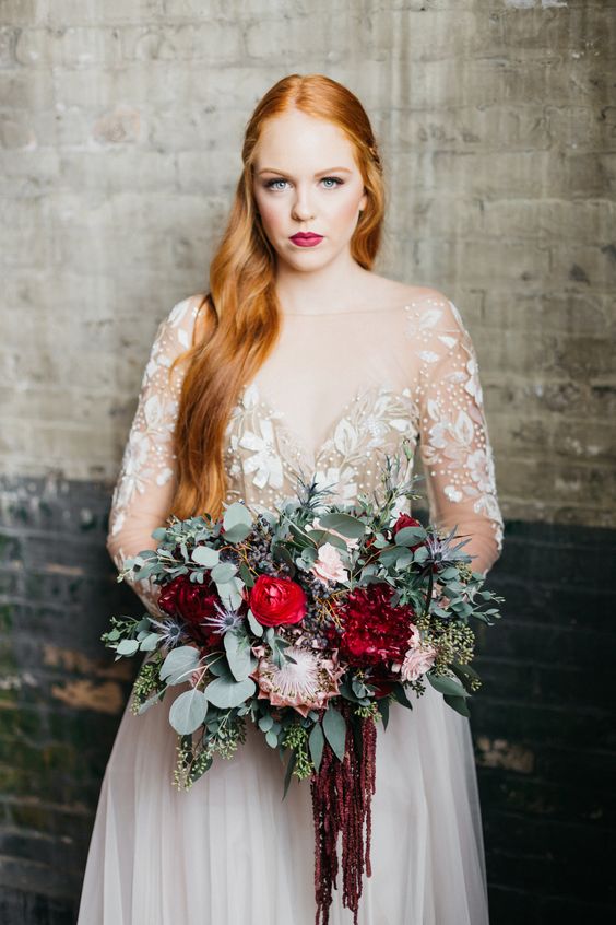 an elegant winter wedding bouquet of greenery, blush, red and burgundy blooms and thistles