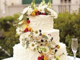a lovely summer wedding cake covered with white textural buttercream, with greenery, berries, fruit and some wildflowers is ideal for a boho wedding