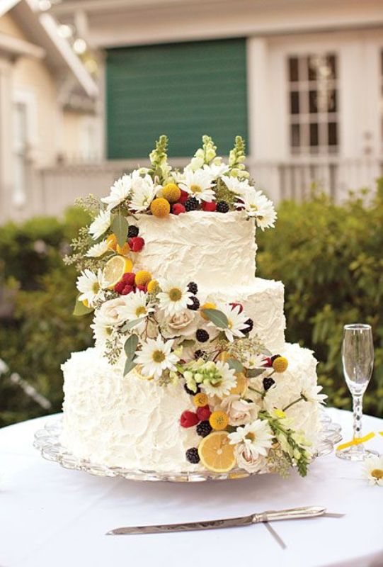 A lovely summer wedding cake covered with white textural buttercream, with greenery, berries, fruit and some wildflowers is ideal for a boho wedding