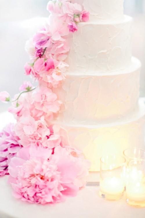 a dreamy white textural buttercream wedding cake with light pink and bolder pink blooms descending the cake for a spring or summer wedding