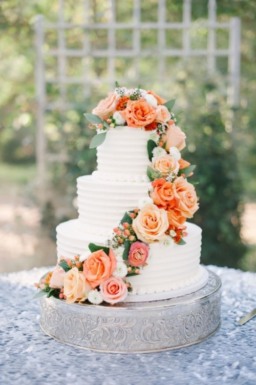 a textural white buttercream wedding cake decorated with orange and peachy roses and greenery is a cool and bold idea for summer