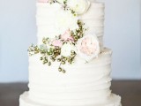 a white textural buttercream wedding cake decorated with white and blush blooms and gold berries looks amazing